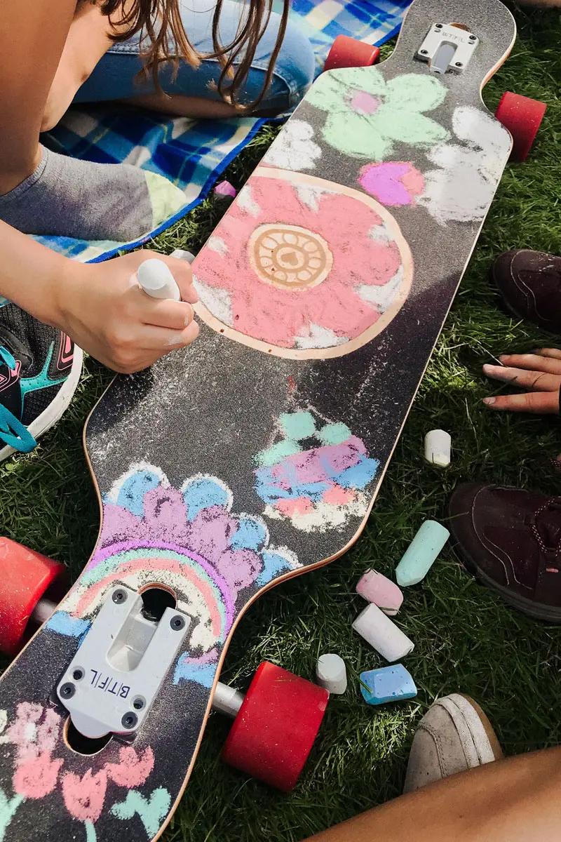 Ein Longboard ist auf dem Schoß eines Kindes, von oben mit bunter Kreide bemalt