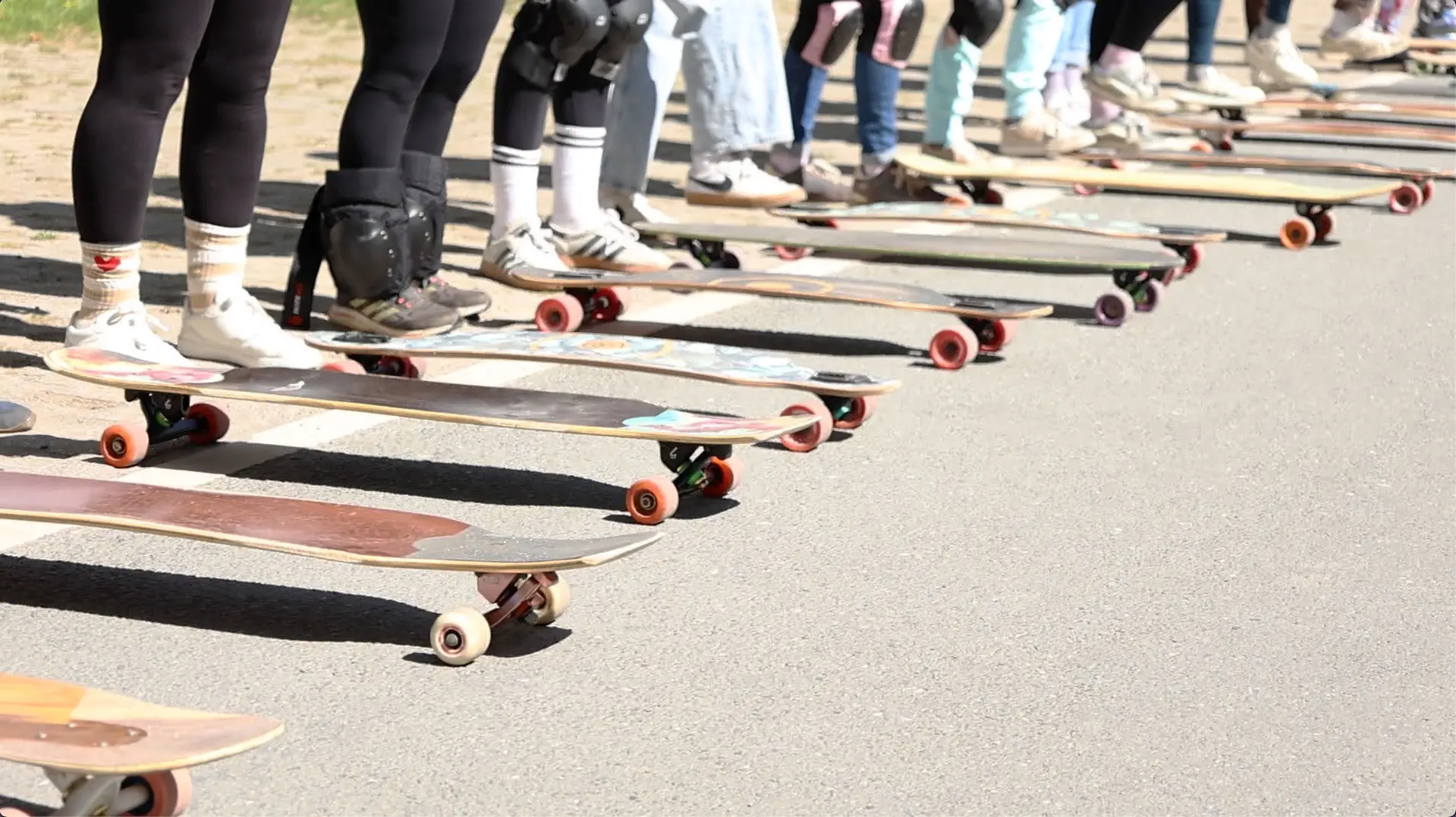 Von links nach rechts sind Füße zu sehen, davor ist jeweils ein Longboard positioniert.